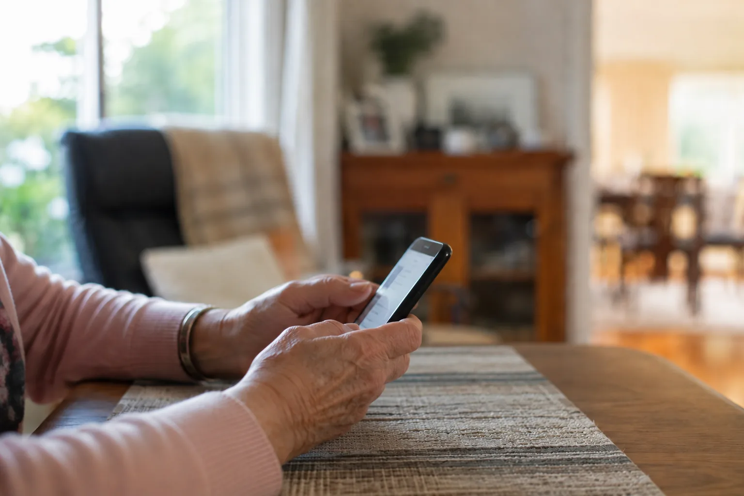 Older Australian holding a phone in a warm living room